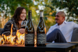 Argyle duo in front of fire with wine