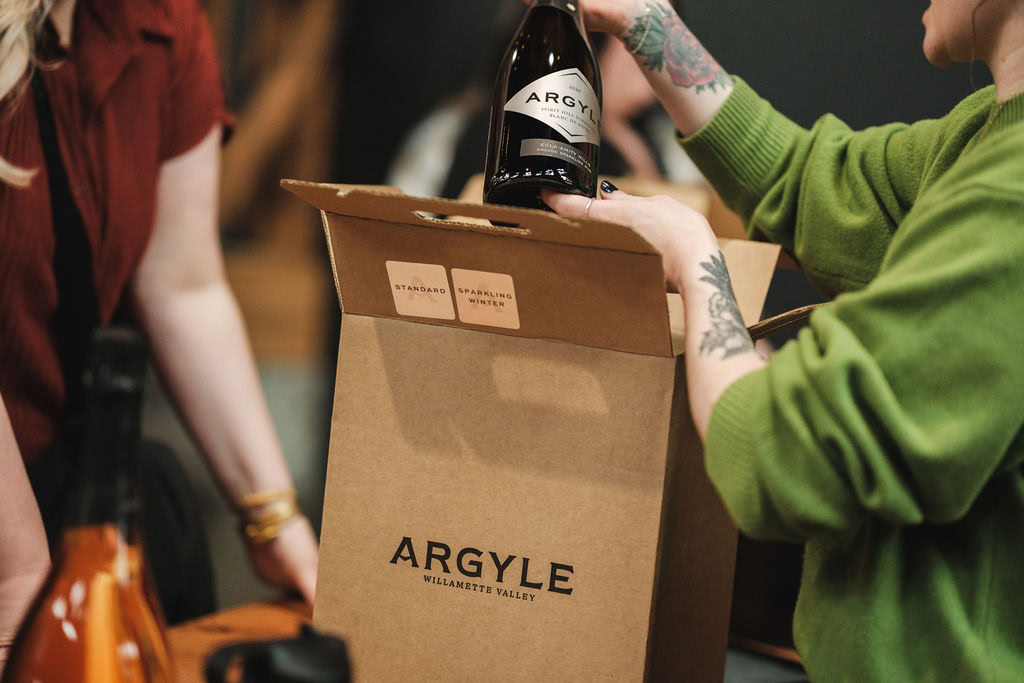 Close-up of a person holding two chilled bottles of Argyle sparkling wine—Blanc de Noirs and Brut Rosé—surrounded by other bottles in an ice bucket.